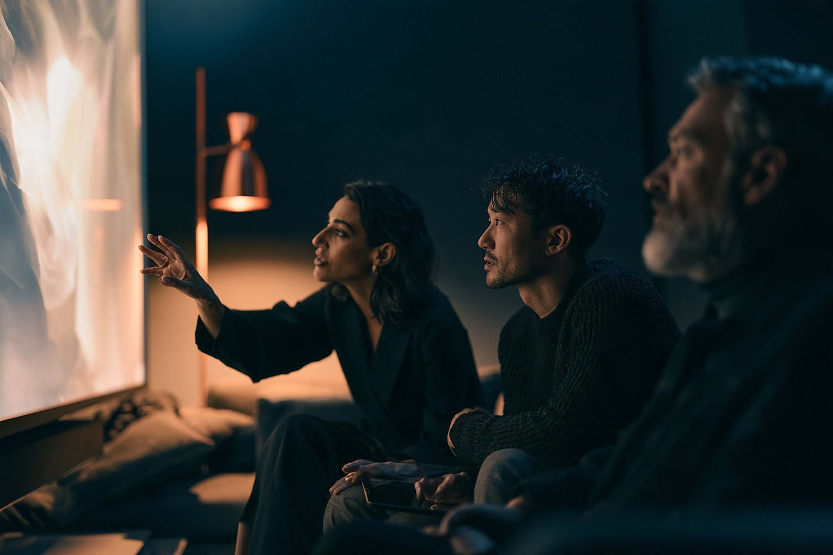 Three people review a first edit on a large screen; the client lead gestures as she gives direction.